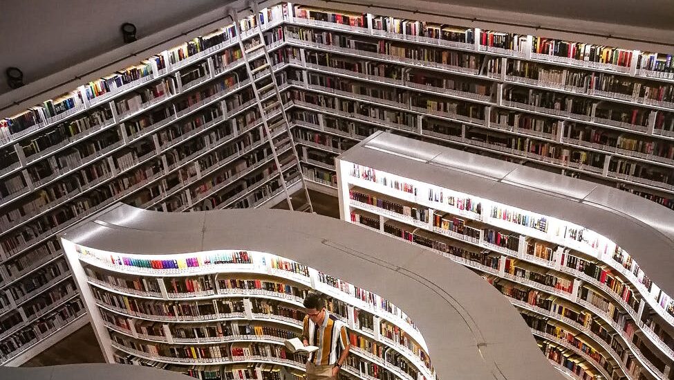 man standing inside library while reading book